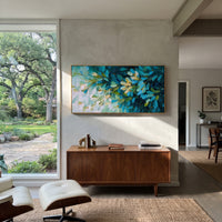 "Teal Green Leaf Branch Painting" focuses on atmosphere, surface movement, and sculptural heavy impasto craftsmanship rather than a fixed literal storyline. The composition uses this hand-painted panoramic canvas presents a close view of leafy branches in deep teal blue, green, cream white, and small golden accents, with visible raised palette-knife texture as the visual anchor, while layered palette-knife paint, raised plaster-like texture, and softened brush movement create tactile depth