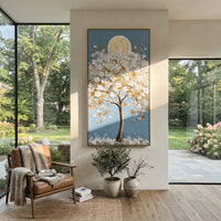 "Moonlit White Blossom Tree Painting" focuses on atmosphere, surface movement, and sculptural heavy impasto craftsmanship rather than a fixed literal storyline. The composition uses this hand-painted vertical canvas presents a tall tree covered in raised white blossoms and golden leaves, set before a soft round moon on a clear blue background as the visual anchor, while layered palette-knife paint, raised plaster-like texture, and softened brush movement create tactile depth across the canvas.