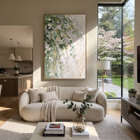 "White Green Floral Branch Painting" focuses on atmosphere, surface movement, and sculptural heavy impasto craftsmanship rather than a fixed literal storyline. The composition uses this hand-painted vertical canvas presents white raised blossoms and green leaves trailing diagonally over a pale textured wall, with thin brown branches and soft gold touches as the visual anchor, while layered palette-knife paint, raised plaster-like texture, and softened brush movement create tactile depth across