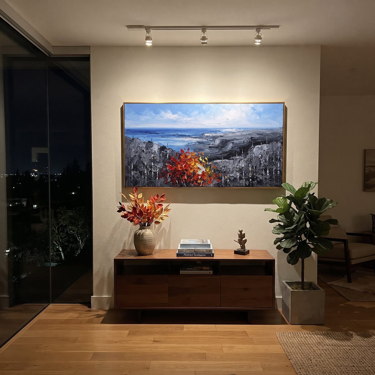 "Blue Coast Autumn Painting" focuses on atmosphere, surface movement, and sculptural heavy impasto craftsmanship rather than a fixed literal storyline. The composition uses this hand-painted panoramic canvas shows an open blue shoreline and grey rocky headlands, anchored by a thick red orange autumn tree and dark textured woodland in the foreground as the visual anchor, while layered palette-knife paint, raised plaster-like texture, and softened brush movement create tactile depth across the