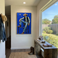 "Blue Star Cowboy Chair Painting" focuses on atmosphere, surface movement, and sculptural heavy impasto craftsmanship rather than a fixed literal storyline. The composition uses this hand-painted vertical canvas depicts a cowboy sitting on a high chair against a vivid blue field with yellow stars as the visual anchor, while layered palette-knife paint, raised plaster-like texture, and softened brush movement create tactile depth across the canvas. Curated with a balanced blue, beige, black