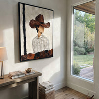 "Side Glance Brown Hat Painting" focuses on atmosphere, surface movement, and sculptural heavy impasto craftsmanship rather than a fixed literal storyline. The composition uses this hand-painted vertical canvas shows a faceless western figure turned slightly to the side under a wide brown hat as the visual anchor, while layered palette-knife paint, raised plaster-like texture, and softened brush movement create tactile depth across the canvas. Curated with a balanced beige, brown, black palette
