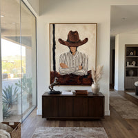 "Arms Crossed Brown Hat Cowboy Painting" focuses on atmosphere, surface movement, and sculptural heavy impasto craftsmanship rather than a fixed literal storyline. The composition uses this hand-painted vertical canvas shows a faceless cowboy standing with crossed arms beneath a broad brown hat as the visual anchor, while layered palette-knife paint, raised plaster-like texture, and softened brush movement create tactile depth across the canvas. Curated with a balanced beige, brown, black