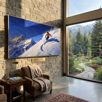 Orange Powder Turn Skier focuses on a single orange skier carving a blue shadowed turn across a ridge. The artwork shows a winter ski scene built from the actual image: visible downhill figures, curved snow tracks, raised ridgelines, and alpine space arranged in a wide composition. The blue, orange, white palette gives the piece a cold mountain atmosphere while the thick impasto surface creates shadows along each snowbank, ski line, and textured ridge. This is presented as hand-painted textured