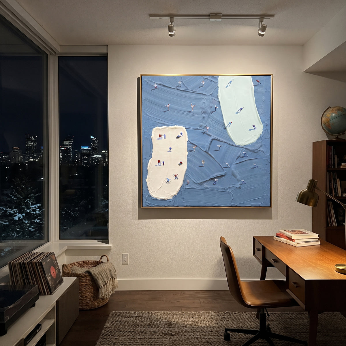 Blue Resort Island Trails focuses on tiny skiers scattered across blue resort trails divided by two pale raised ski islands. The artwork shows a winter ski scene built from the actual image: visible downhill figures, curved snow tracks, raised ridgelines, and alpine space arranged in a balanced composition. The blue, white, gray palette gives the piece a cold mountain atmosphere while the thick impasto surface creates shadows along each snowbank, ski line, and textured ridge. This is presented