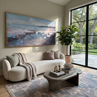 This 100% hand-painted coastal landscape features this hand-painted horizontal canvas captures a soft blue shoreline with pale surf, distant land, and muted pink grey reflections. The gentle coastal landscape brings a relaxed atmosphere to living rooms, bedrooms, offices, beach houses, and hospitality interiors. The composition uses wide horizontal bands of sky, water, and shore with thick but softened palette knife texture. Its horizontal format fits above sofas, beds, and long console walls.
